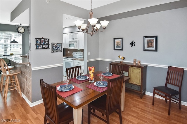 dining room with light wood-style floors, a notable chandelier, and baseboards