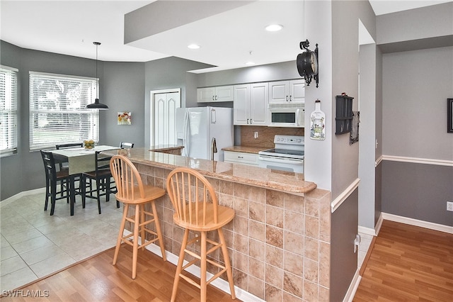 kitchen featuring white appliances, baseboards, light wood-style floors, a kitchen breakfast bar, and tasteful backsplash