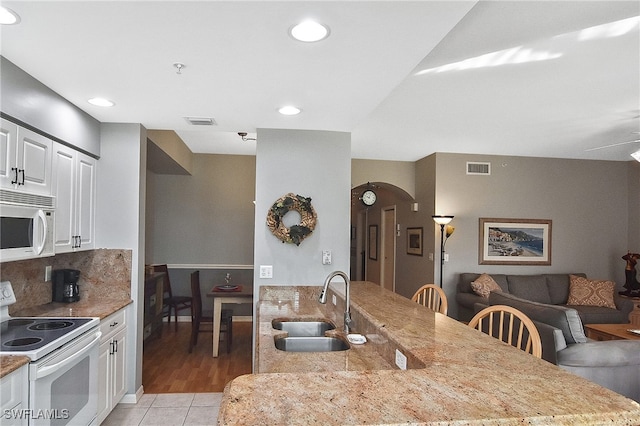 kitchen featuring white cabinetry, sink, a kitchen bar, light stone counters, and white appliances