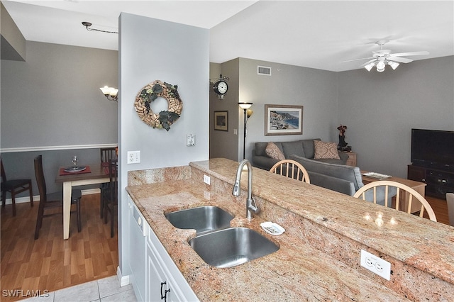 kitchen with ceiling fan, a sink, white cabinetry, visible vents, and light stone countertops