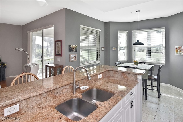 kitchen featuring white cabinetry, sink, hanging light fixtures, light stone counters, and a healthy amount of sunlight