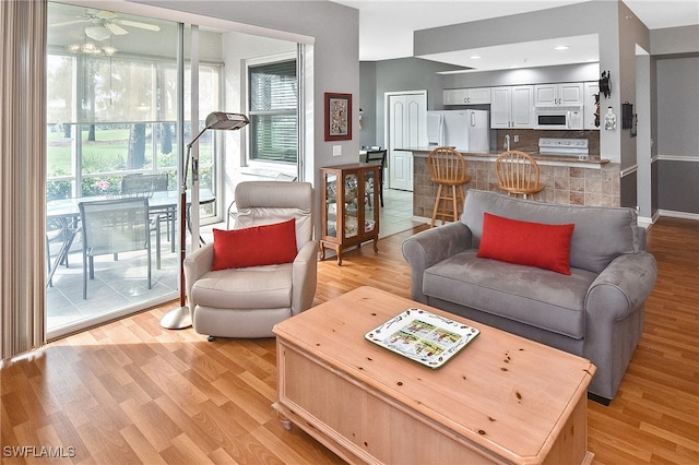 living area featuring ceiling fan, light wood-style flooring, and baseboards