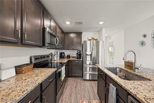 kitchen with sink, stainless steel appliances, light stone counters, dark brown cabinetry, and light wood-type flooring