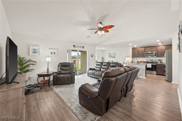 living room with ceiling fan, light hardwood / wood-style floors, and vaulted ceiling