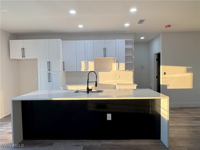 kitchen with white cabinets, dark wood-type flooring, an island with sink, sink, and backsplash