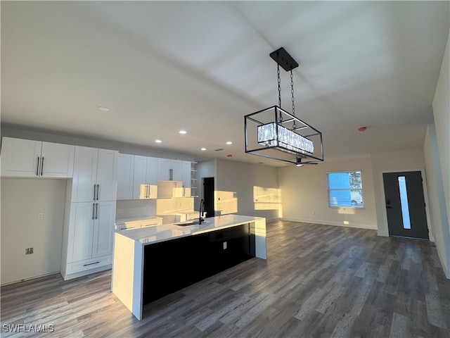 kitchen with wood-type flooring, white cabinetry, sink, pendant lighting, and a center island with sink