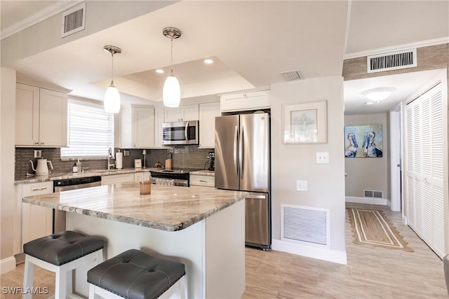 kitchen featuring appliances with stainless steel finishes, hanging light fixtures, a tray ceiling, white cabinets, and a kitchen island