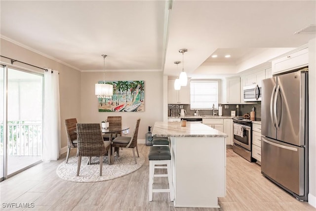 kitchen with a kitchen island, appliances with stainless steel finishes, decorative light fixtures, white cabinetry, and light stone counters