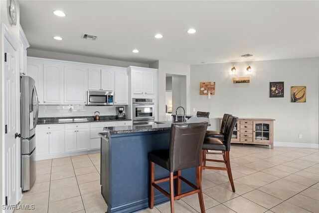 kitchen featuring a kitchen bar, stainless steel appliances, white cabinets, light tile patterned flooring, and decorative backsplash