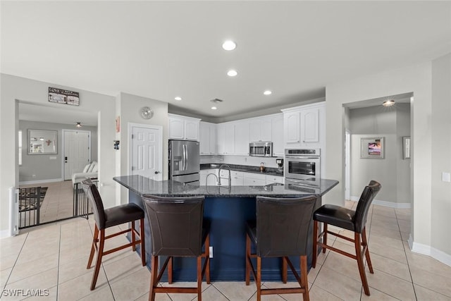 kitchen featuring light tile patterned floors, stainless steel appliances, white cabinets, a kitchen bar, and dark stone counters