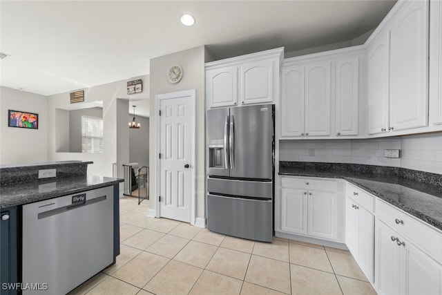 kitchen with appliances with stainless steel finishes, backsplash, white cabinets, light tile patterned floors, and dark stone countertops