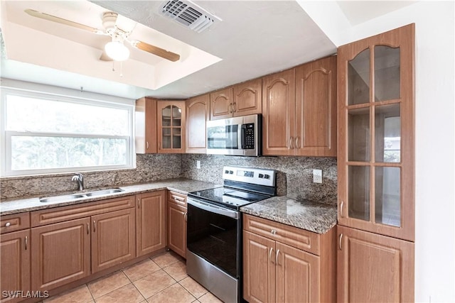 kitchen with stone countertops, a raised ceiling, sink, light tile patterned floors, and stainless steel appliances