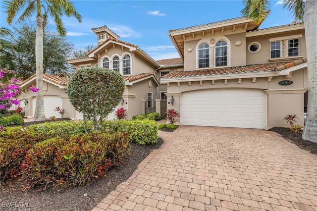 mediterranean / spanish home featuring a garage, decorative driveway, a tile roof, and stucco siding