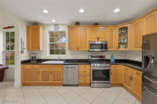 kitchen with recessed lighting, a sink, appliances with stainless steel finishes, dark countertops, and glass insert cabinets