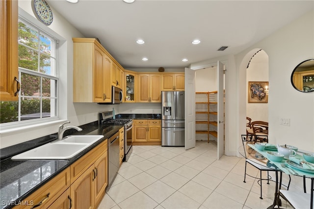 kitchen with dark stone countertops, sink, light tile patterned floors, and appliances with stainless steel finishes