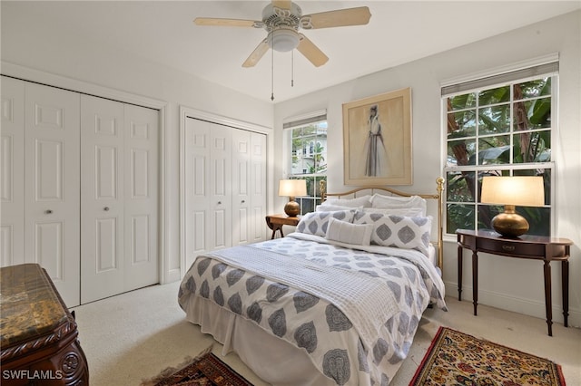 bedroom featuring ceiling fan, light colored carpet, and two closets