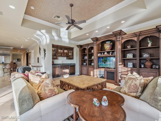 living room with a raised ceiling, ornamental molding, wet bar, and ceiling fan