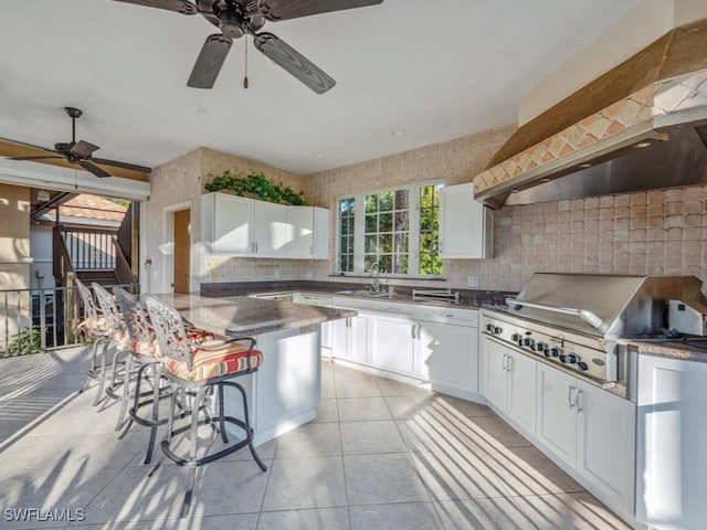 kitchen featuring a breakfast bar, custom exhaust hood, white cabinetry, light tile patterned floors, and backsplash