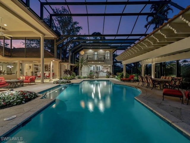 pool at dusk featuring an outdoor hangout area, a patio area, ceiling fan, and glass enclosure