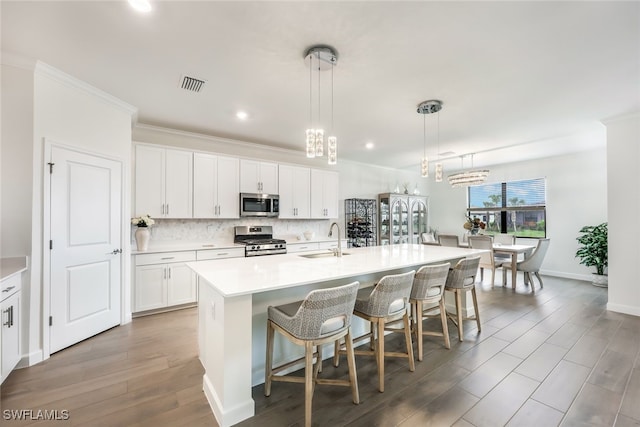 kitchen with pendant lighting, appliances with stainless steel finishes, sink, white cabinets, and an island with sink