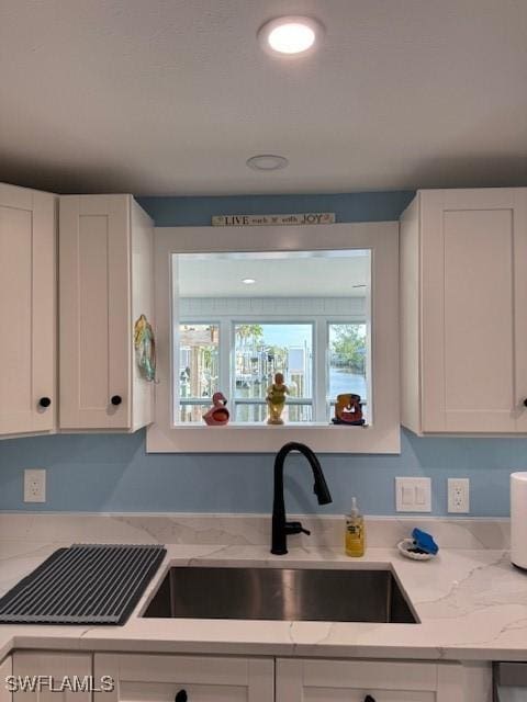 kitchen featuring light stone countertops, white cabinets, and a sink