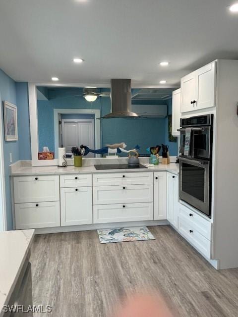 kitchen with island range hood, light wood-style flooring, black electric stovetop, double oven, and white cabinetry