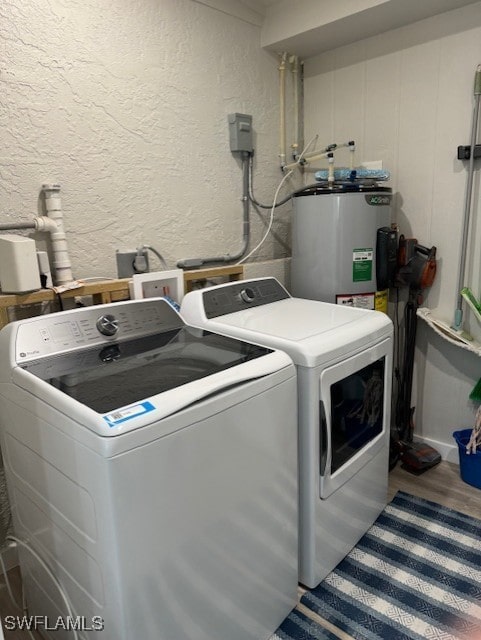 clothes washing area featuring washing machine and clothes dryer, water heater, a textured wall, wood finished floors, and laundry area