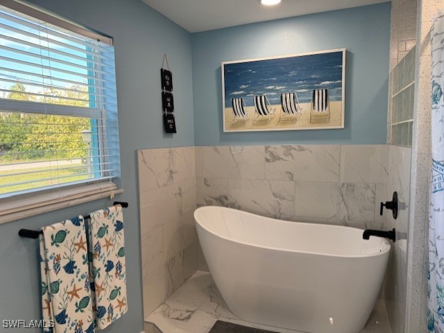 bathroom with a freestanding bath, marble finish floor, and wainscoting