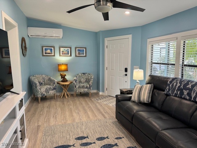 living room with baseboards, a ceiling fan, a wall unit AC, lofted ceiling, and wood finished floors