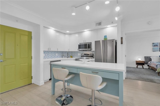 kitchen with stainless steel appliances, ornamental molding, white cabinets, and decorative backsplash