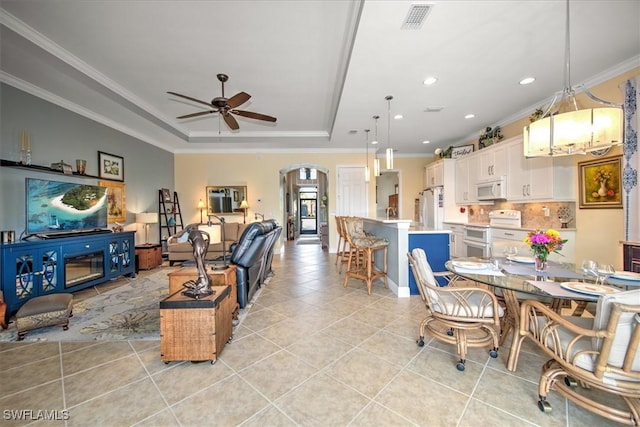 tiled living room with ceiling fan, a raised ceiling, and ornamental molding