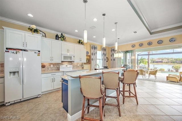 kitchen with hanging light fixtures, white cabinets, white appliances, ornamental molding, and a center island with sink