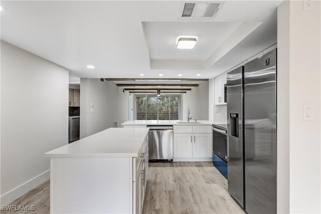 kitchen with sink, white cabinetry, light wood-type flooring, a raised ceiling, and stainless steel appliances