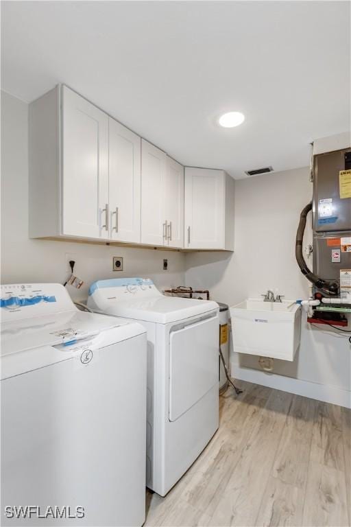 washroom featuring sink, cabinets, heating unit, light hardwood / wood-style floors, and washer and dryer