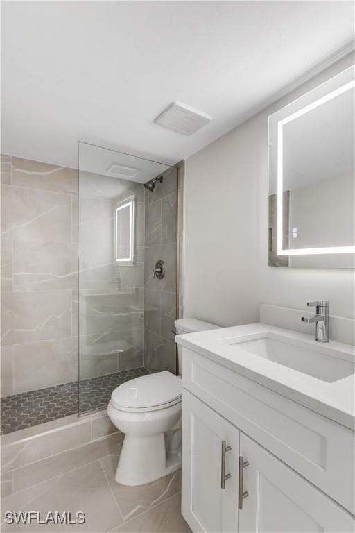 bathroom with tile patterned flooring, vanity, a tile shower, and toilet