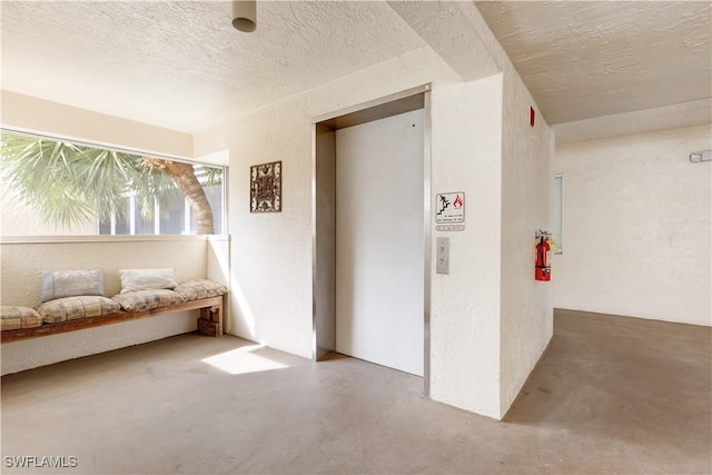 corridor featuring elevator, concrete floors, and a textured ceiling