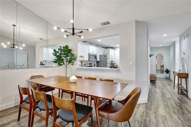 dining space with an inviting chandelier, light hardwood / wood-style flooring, and a textured ceiling