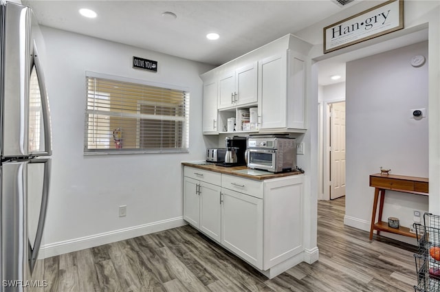 kitchen featuring stainless steel refrigerator, butcher block countertops, light hardwood / wood-style flooring, and white cabinets