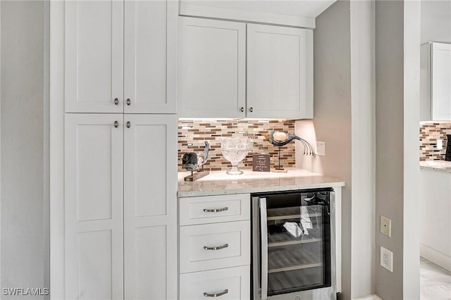 bar with wine cooler, backsplash, light stone counters, and white cabinets