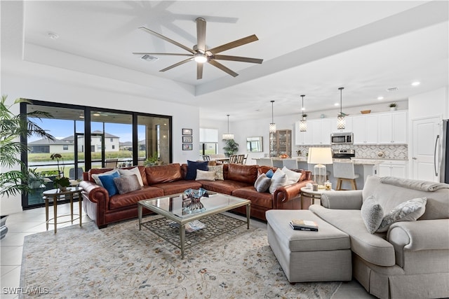 living room with ceiling fan, a raised ceiling, and light tile patterned floors