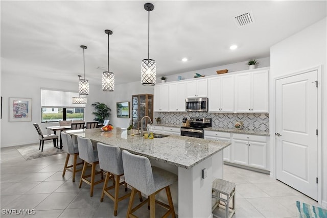 kitchen featuring appliances with stainless steel finishes, decorative light fixtures, an island with sink, sink, and white cabinets