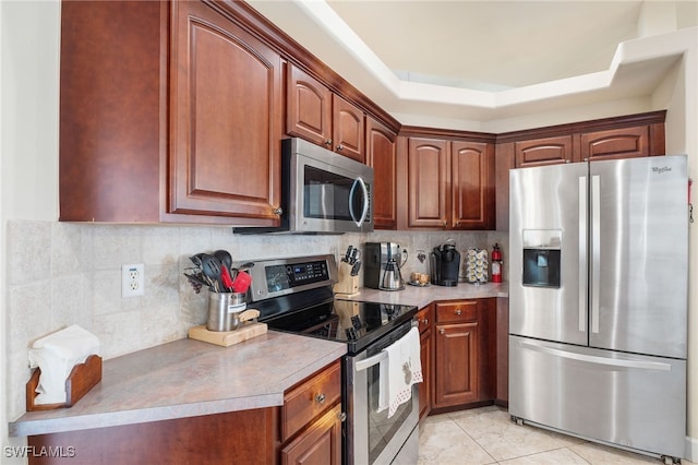 kitchen featuring a raised ceiling, light tile patterned flooring, appliances with stainless steel finishes, and decorative backsplash