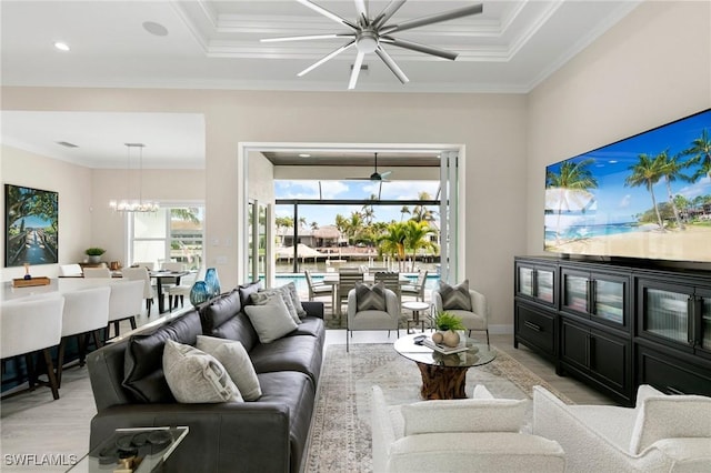 living room with ceiling fan with notable chandelier, crown molding, light hardwood / wood-style floors, and a tray ceiling