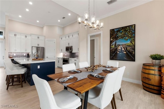 dining area with sink, an inviting chandelier, light hardwood / wood-style floors, and crown molding