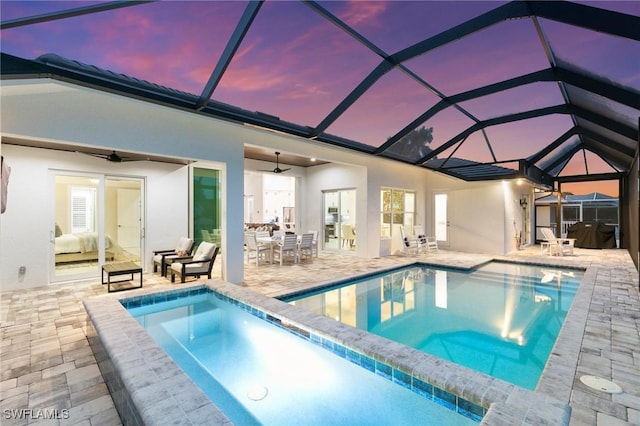 pool at dusk featuring ceiling fan, a patio, a lanai, and a hot tub