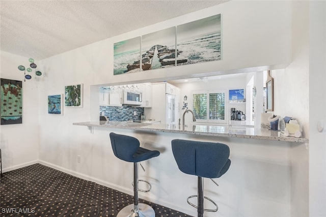 kitchen featuring backsplash, a kitchen breakfast bar, a textured ceiling, white cabinets, and dark carpet