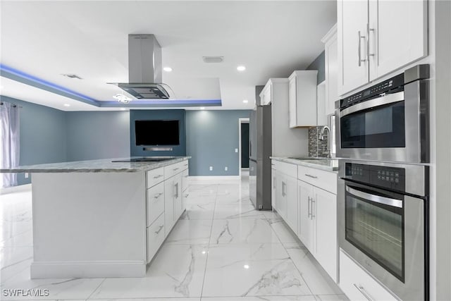 kitchen featuring white cabinetry, a center island, stainless steel refrigerator, a raised ceiling, and island exhaust hood