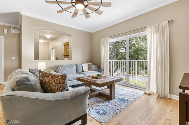 living area with wood finished floors, a ceiling fan, ornamental molding, baseboards, and arched walkways