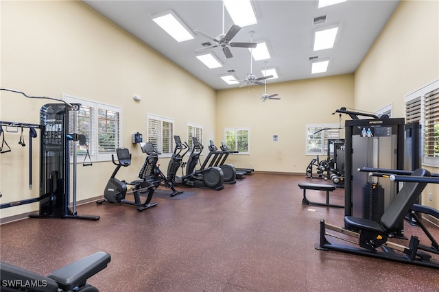 exercise room with ceiling fan, a skylight, and a high ceiling