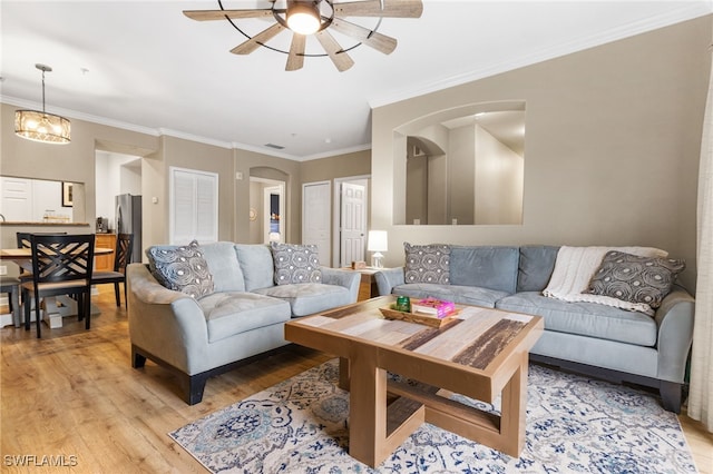 living area with light wood-style flooring, ceiling fan, ornamental molding, and arched walkways